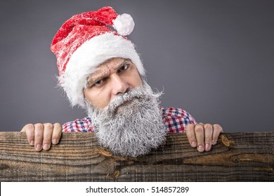 Closeup of a  man with frozen beard wearing santa red cap  and looking over the fence.Winter and Christmas time