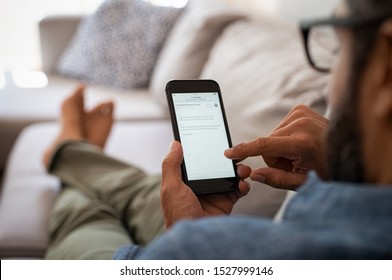 Closeup of a man hand holding cellphone with internet browser on screen. Man with spectacles relaxing sitting on couch. Closeup of mature latin man using smartphone to checking email at home.