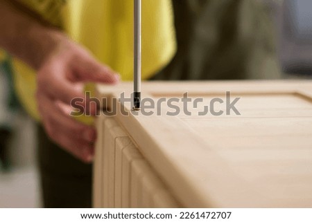 Closeup man hand using manual screwdriver and screwing screw in board. Assembling new wooden furniture.