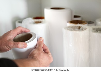 Close-up of man hands choosing white printing paper roll with bunch of wide format paper rolls blurred in background