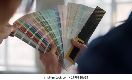 Closeup Man Hands Holding Swatches Book On Blurred Background. Unknown People Choosing Color For Walls In New House. Unrecognizable Couple Using Color Palette For Home Decoration Indoors.