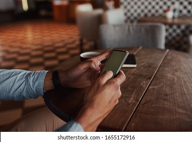 Closeup of man hands using smartphone while sitting in cafe drinking coffee using touchscreen
