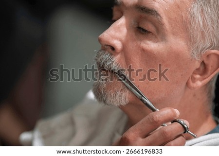 Close-up of man having mustache precisely trimmed with professional scissors at modern barbershop