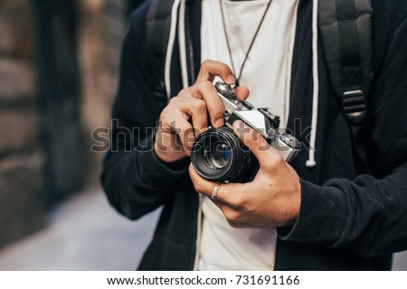 Closeup of man in hipster outfit, black hoodie cardigan and white tshirt, holding vintage analog film camera, zooming and focusing