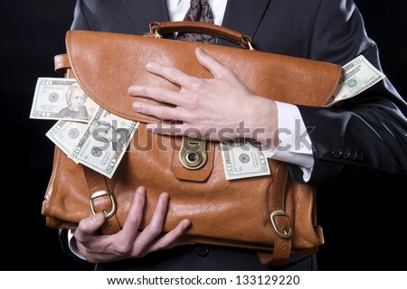 Closeup of man holding briefcase with money spilling out close to his chest
