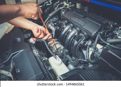 Closeup of man holding dipstick while checking level the oil in the car engine on the roadside. Mechanic open hood with auto maintenance repair service. Need assistance help with the machine.