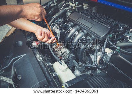 Closeup of man holding dipstick while checking level the oil in the car engine on the roadside. Mechanic open hood with auto maintenance repair service. Need assistance help with the machine.
