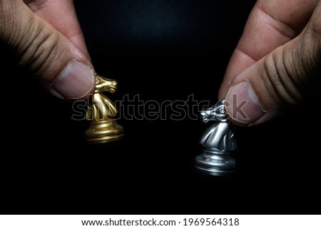 Close-up of a man holding a golden and silver chess horse on a chessboard, copying spaces for your message.