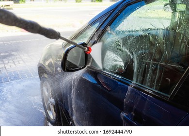 Nahaufnahme eines Mannes, der einen Hochdruckspritzer für das Waschen von Autos hält. Unberührte Selbstbedienungswaschung des Autos. Konzeption der Desinfektion und antiseptische Reinigung des Fahrzeugs, Corvid-19 und Coronavirus