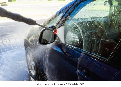Nahaufnahme eines Mannes, der einen Hochdruckspritzer für das Waschen von Autos hält. Unberührte Selbstbedienungswaschung des Autos. Konzeption der Desinfektion und antiseptische Reinigung des Fahrzeugs, Corvid-19 und Coronavirus