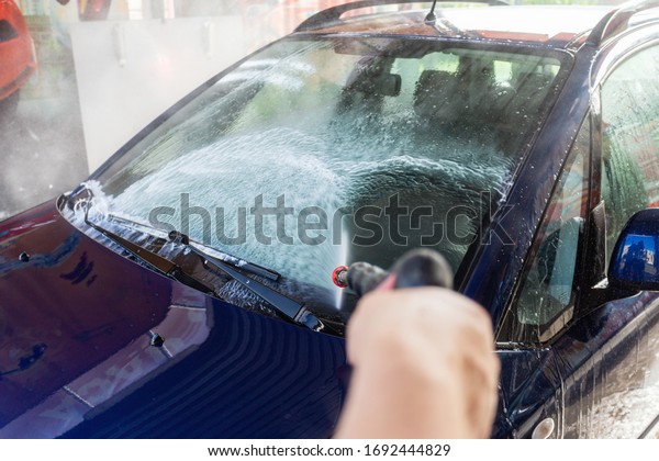 Close-up man holding a high-pressure water\
sprayer for car front window washing. Contactless self-service car\
wash. Concept disinfection and antiseptic cleaning of vehicle,\
corvid-19 and\
coronavirus