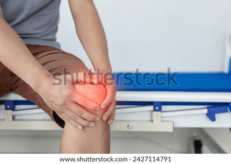 Close-up of a man holding his knee in discomfort. Suffering from knee pain while sitting on bed at home Health concept, knee pain after exercise in arthritis concept.