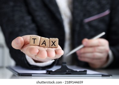 Close-up Of Man Holding On Palm Tax Word Collected Of Wooden Blocks Letters. Government, State Taxes, Calculation Individual Income And Tax Laws Concept