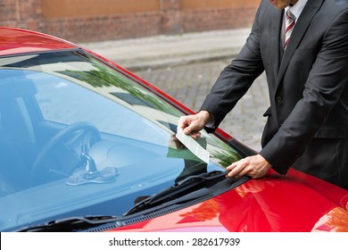 Close-up Of A Man Holding A Parking Ticket Placed On Car Windscreen