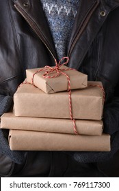 Closeup of a man holding a stack of plain paper wrapped christmas presents. Man is unrecognizable wearing a sweater and leather jacket.