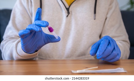 Close-up of man holding a swap sample in lysis buffer home tests for Covid19 with antigen kit. Person wearing latex gloves to collect a possible positive coronavirus sample during the pandemic.