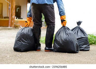 Closeup man holds black plastic bag that contains garbage inside, stand in front of house. Concept : Waste management. Environment problems. Daily chores. Throw away rubbish .                          - Shutterstock ID 2196256485