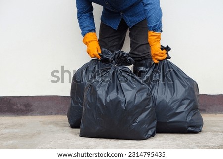 Closeup man holds black plastic bag that contains garbage inside. Concept , Waste management. Environment problems. Daily chores. Throw away rubbish . Sorting type of garbage.                        