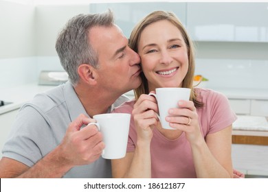 Close-up of a man kissing a happy woman while having coffee in the kitchen at home - Powered by Shutterstock