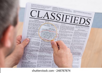 Close-up Of A Man Looking Classifieds Through Magnifying Glass