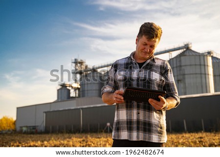 Closeup of man looking at tablet satisfied. Grain silos in background 