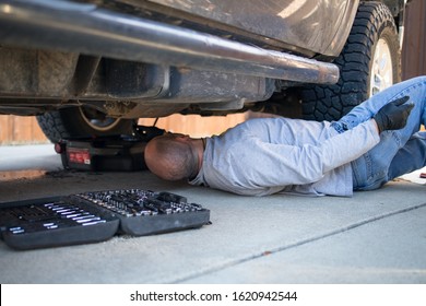 Close-up Of Man Lying Under Truck Emptying The Oil Into An Oil-pan While Doing At-home DIY Oil Change