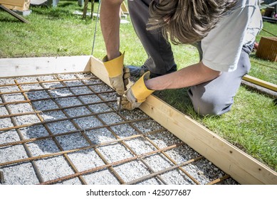 Closeup of a man making a net of steel bars by clipping them together with a wire and pliers placing it in as a reinforcement in a rectangular hole for a concrete foundation outside in backyard. - Shutterstock ID 425077687
