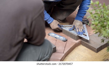 Closeup Of Man Measuring A Red Brick Paver For Cutting To Fit An Edge Along A Rock Boundary