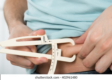 Close-up Of Man Measuring Stomach Fat With Caliper