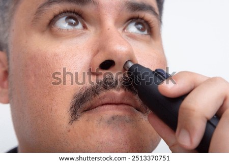 Closeup of a man with a mustache using an electric nose and ear trimmer to groom and cut his nasal hair.