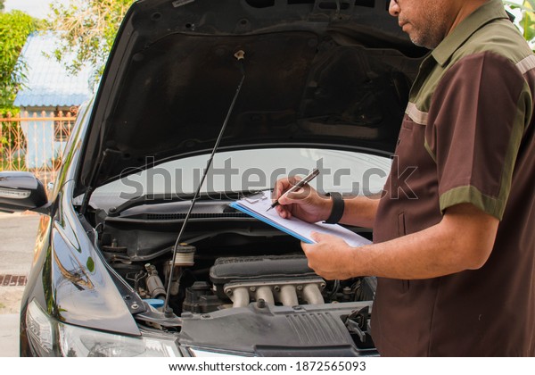 Close-up, A man with a pen is checking a list\
of auto repair parts to fix the cars. Black cars have repair items\
at the garage. Blurred\
background