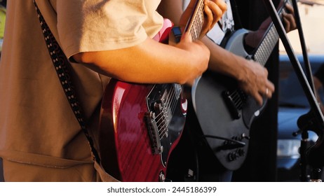 Close-up of a man playing guitar with another guitarist in the background. They are performing together at an outdoor concert. The emphasis is on the interaction between the musician and the guitar - Powered by Shutterstock