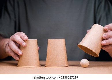 Closeup man playing a shell game, three cups with wooden ball, and reveal where the right position of the ball is