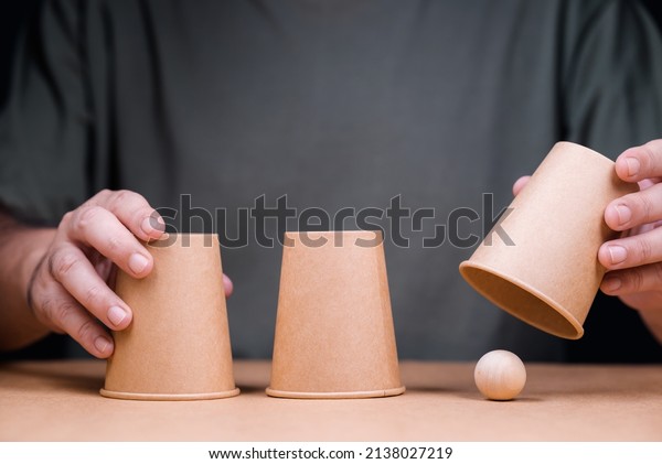 Closeup man\
playing a shell game, three cups with wooden ball, and reveal where\
the right position of the ball\
is