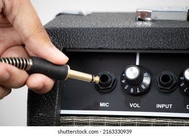 Close-up man is plugging jack cable into amp cabinet.