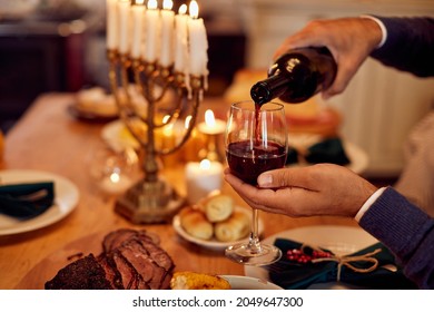 Close-up of man pouring kosher wine into wineglass while celebrating Hanukkah at dining table.