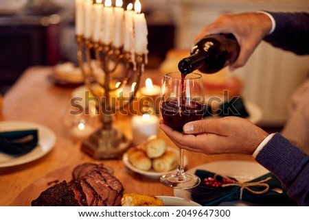 Close-up of man pouring kosher wine into wineglass while celebrating Hanukkah at dining table.
