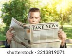 Close-up Of An Man Reading Fake News On Newspaper sitting on a bench in the park