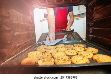 Nahaufnahme eines Mannes in roter Schürze mit frisch gebackenen Keksen aus der Ofenansicht von innen