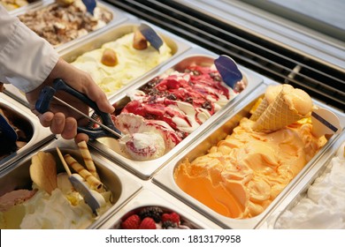 Close-up of a man scooping ice cream from tub in an ice cream parlor.