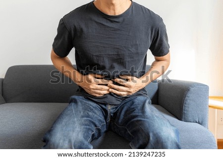 Close-up Of A Man Sitting On Sofa Having a Stomach ache At Home.