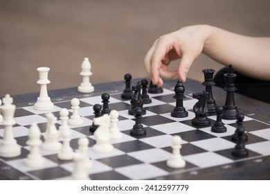 Close-up of a man sitting at a table and playing chess. The teenager picked up a chess piece and makes his move. Outdoor activities