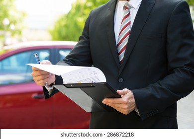 Close-up Of A Man Standing In Front Of Car Holding Clipboard In His Hand