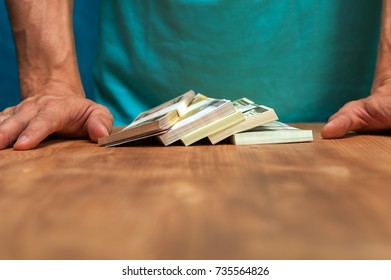Closeup of man standing next to the table with currency heaps. Money cash in male hands.