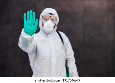 Closeup of man in sterile uniform with rubber gloves standing outdoors and holding hand as a stop sign. Prevention from spreading corona virus concept. - Shutterstock ID 1917546677