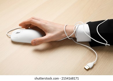 Closeup of man taking computer mouse at wooden table, hand tied with cable. Internet addiction