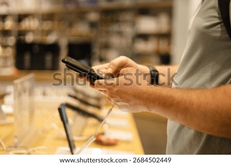 Closeup of man testing smartphone at electronics store. Customer choosing modern gadget from display stand before purchase. Mobile technology and shopping concept.