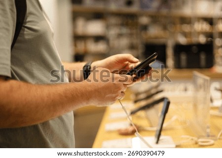 Closeup of man testing smartphone at electronics store. Customer choosing modern gadget from display stand before purchase. Mobile technology and shopping concept.