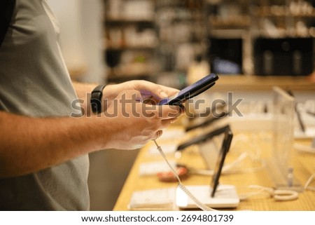 Closeup of man testing smartphone at electronics store. Customer choosing modern gadget from display stand before purchase. Mobile technology and shopping concept.