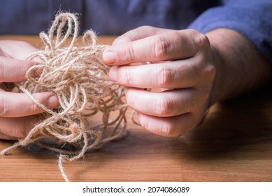 Closeup man try to fix the problem of tangled jute rope, make it easy concept, or psychotherapy